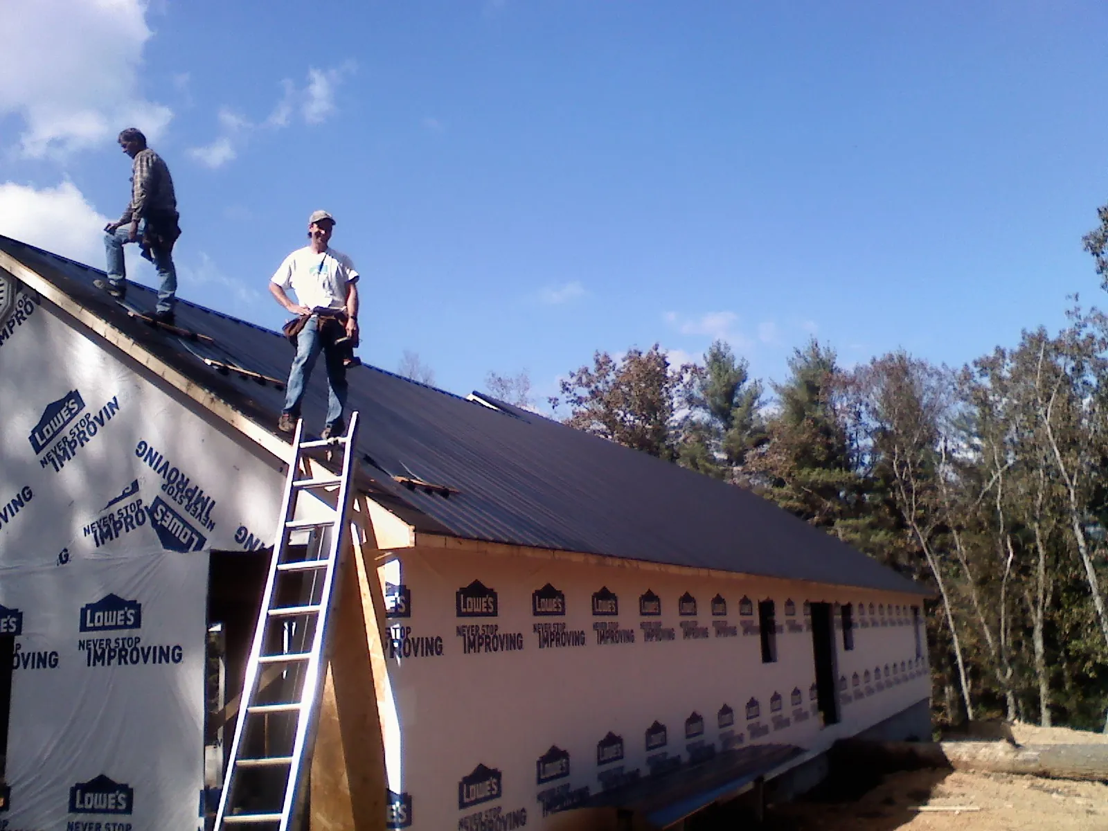 Two roofers standing on a long dark metal roof over a wrapped building in Empire