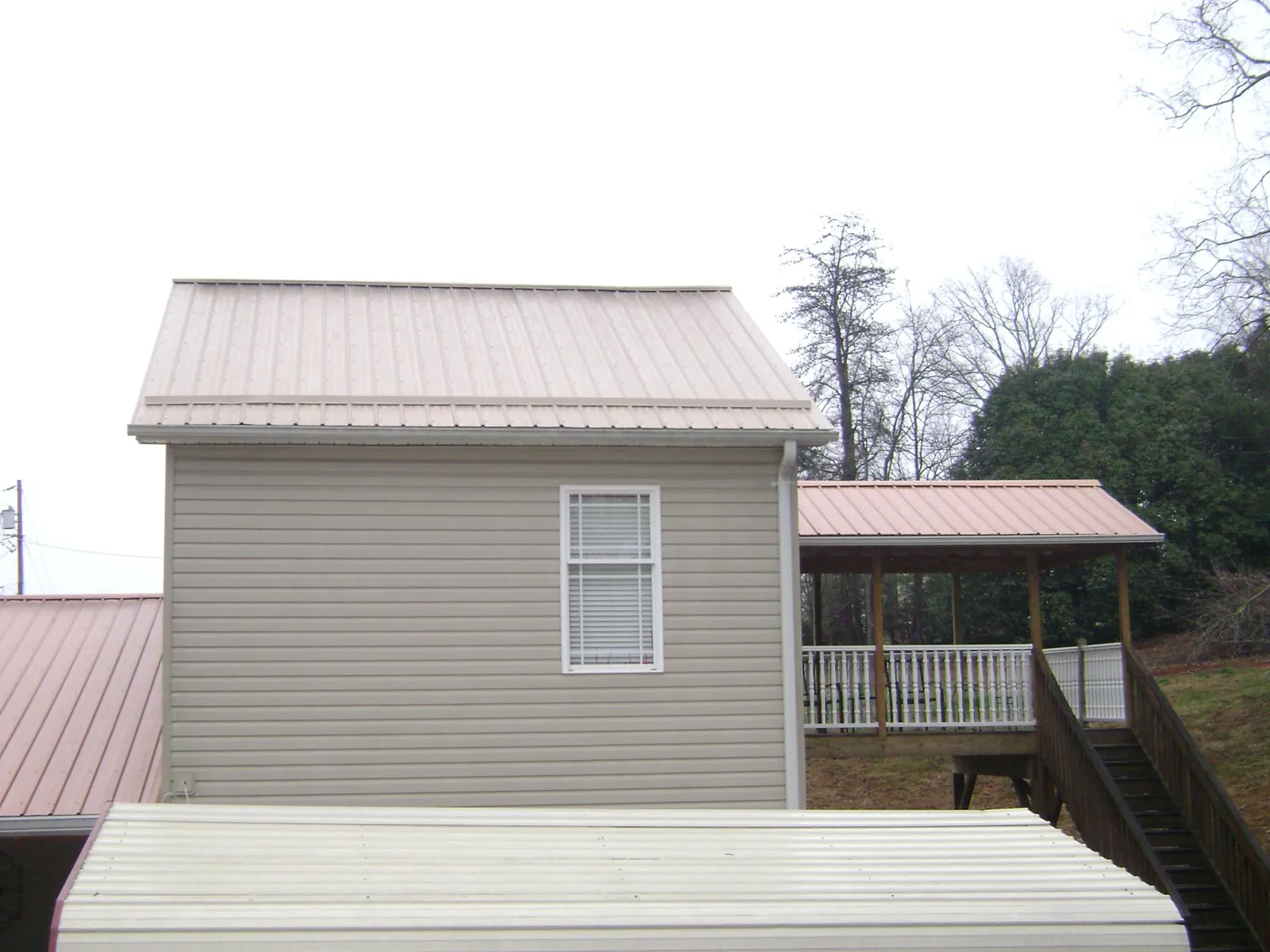 Tan metal roofs on a two story addition and attached porch, from a Roof Replacement job in Empire
